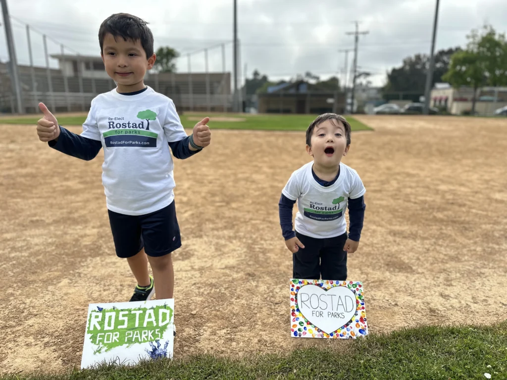 Edison and Roman holding Rostad for Parks signs on a baseball diamond